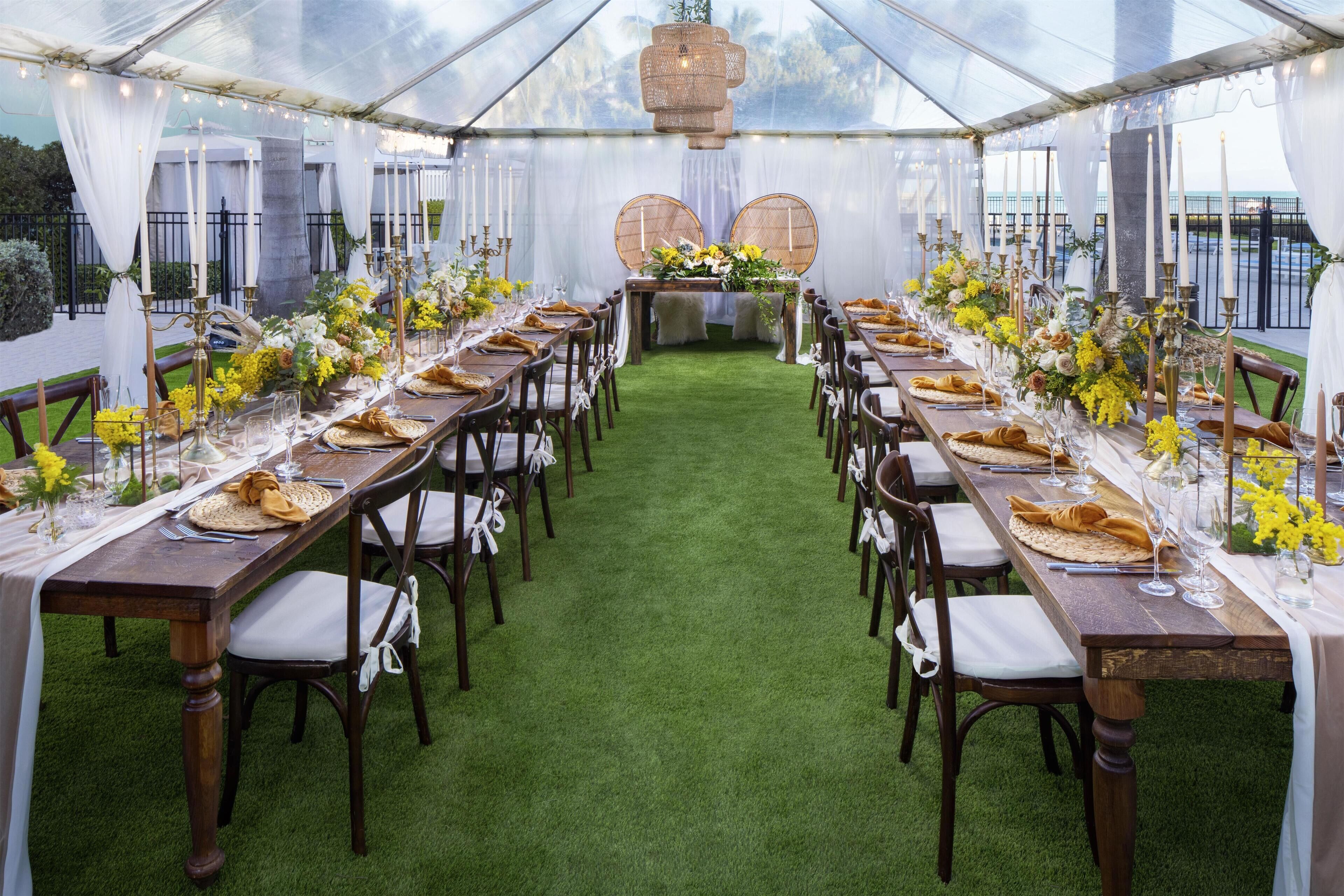 A tented dining area with tables set for a meal, featuring a green carpet and white drapes.
