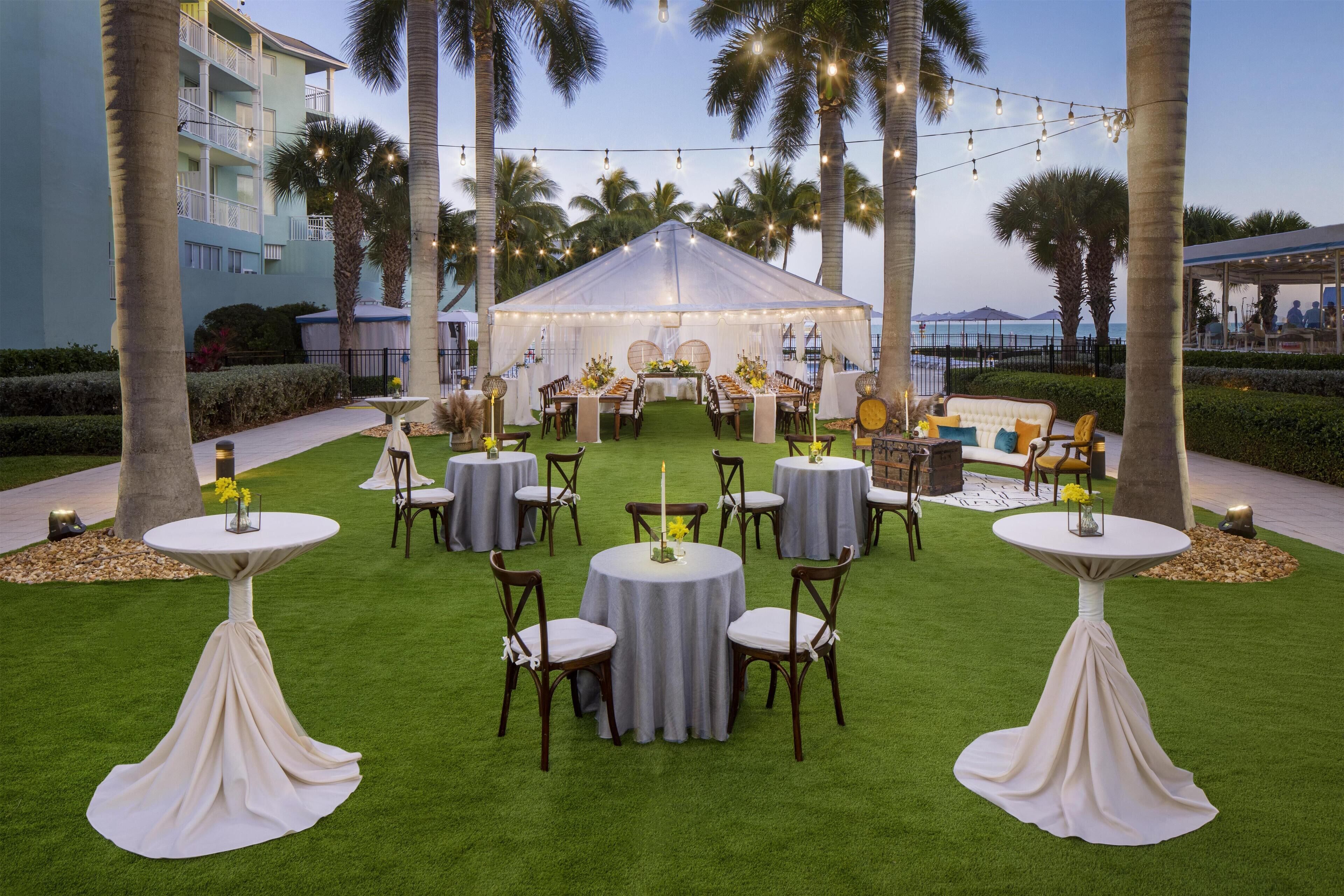 An outdoor event space with a tent, round tables, chairs, and string lights.