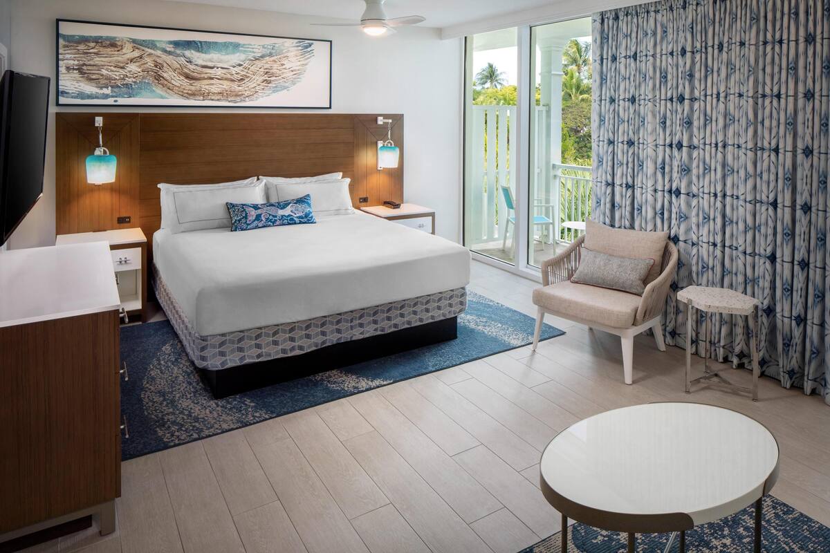 Een moderne hotelkamer met een groot bed, een klein rond tafeltje, een stoel en een balkon met uitzicht op groen.