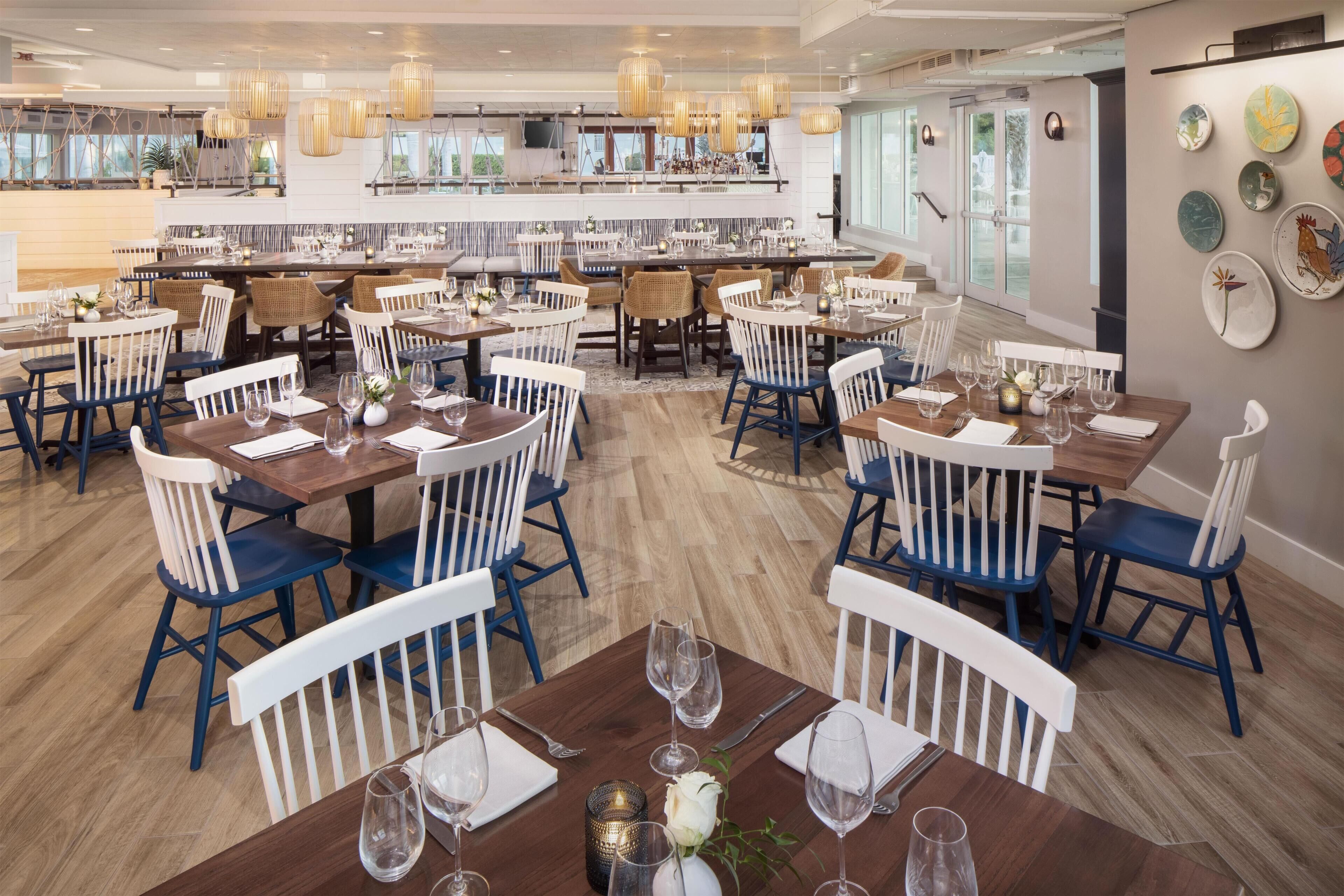 Un restaurante con varias mesas, sillas blancas y azules, y lámparas colgantes.