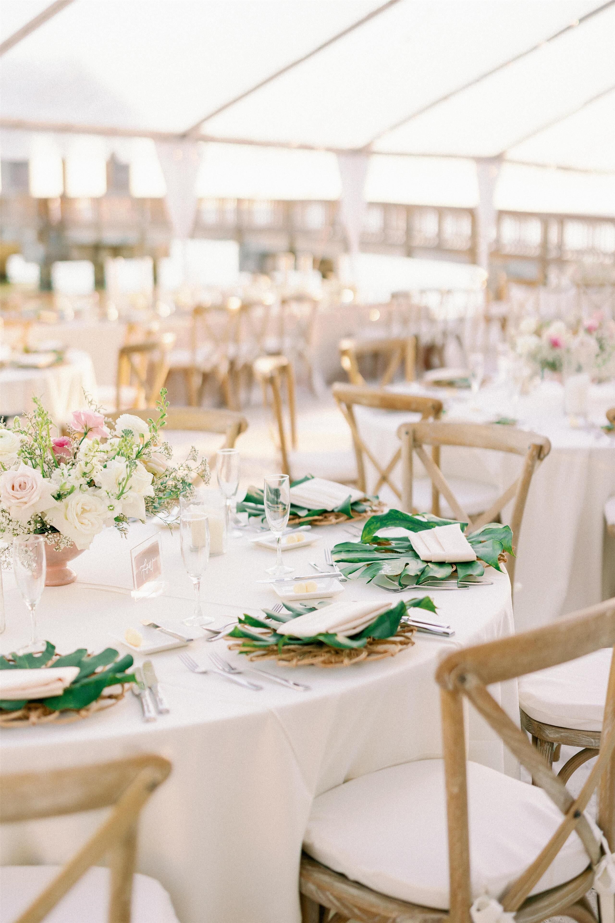 A tented outdoor event space with round tables set with white tablecloths, gold chairs, and floral centerpieces.