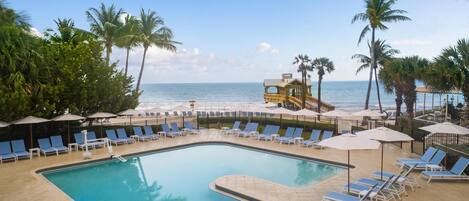 A pool area with lounge chairs and umbrellas, a wooden structure, and palm trees.