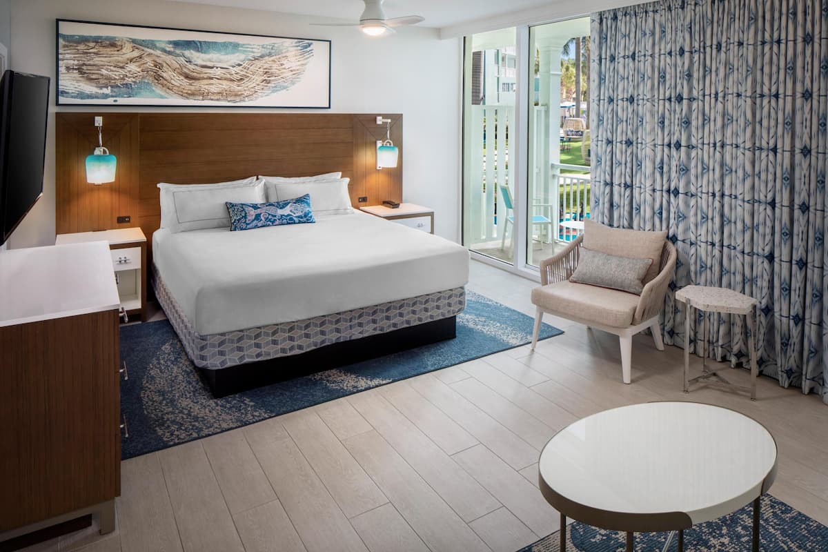 Een moderne hotelkamer met een groot bed, een klein rond tafeltje, een stoel en een balkon met uitzicht.