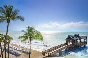 A beach with a wooden pier, palm trees, and beach umbrellas. - The Reach Key West, Curio Collection by Hilton (Key West)