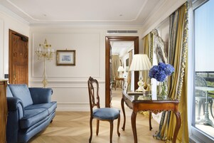 Una stanza con un divano blu, una sedia di legno, un tavolino in vetro con un vaso di fiori e uno specchio grande.