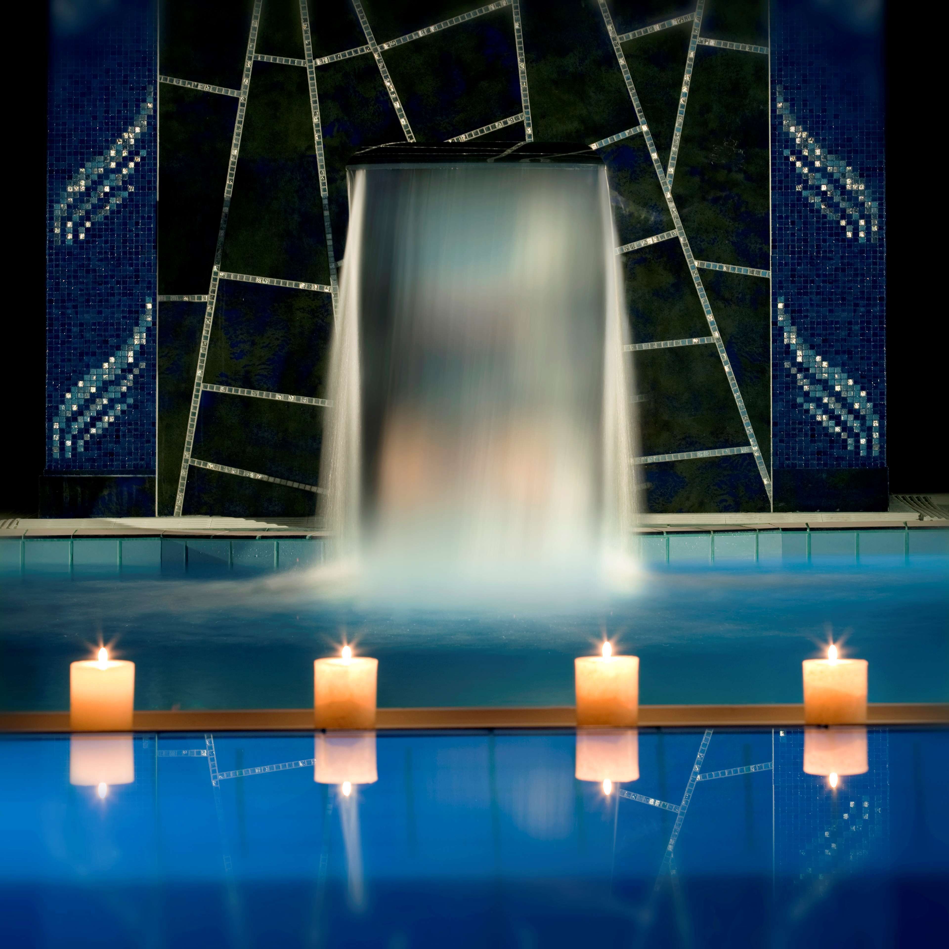 A pool with four candles and a waterfall feature.