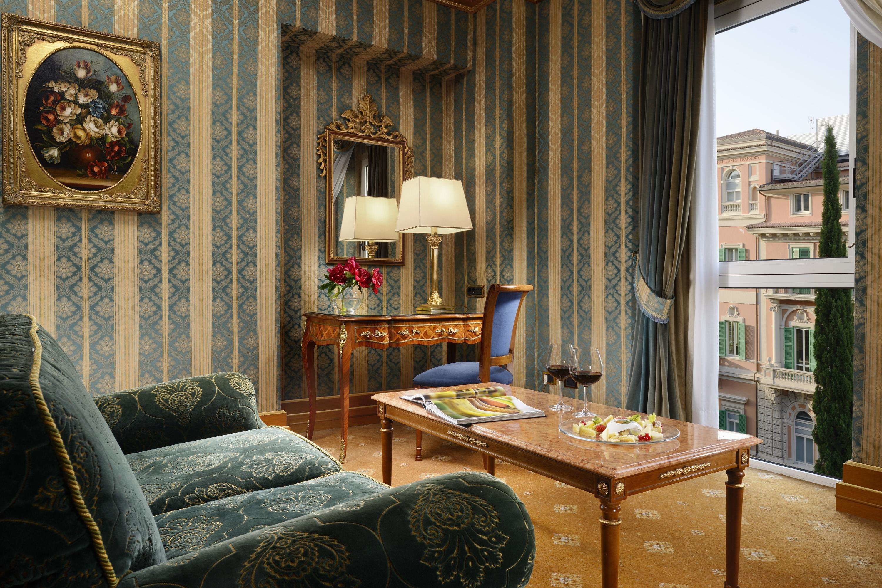 Une pièce avec un canapé, une table sur laquelle se trouve un magazine et un verre de vin, un miroir et une fenêtre donnant sur des immeubles.