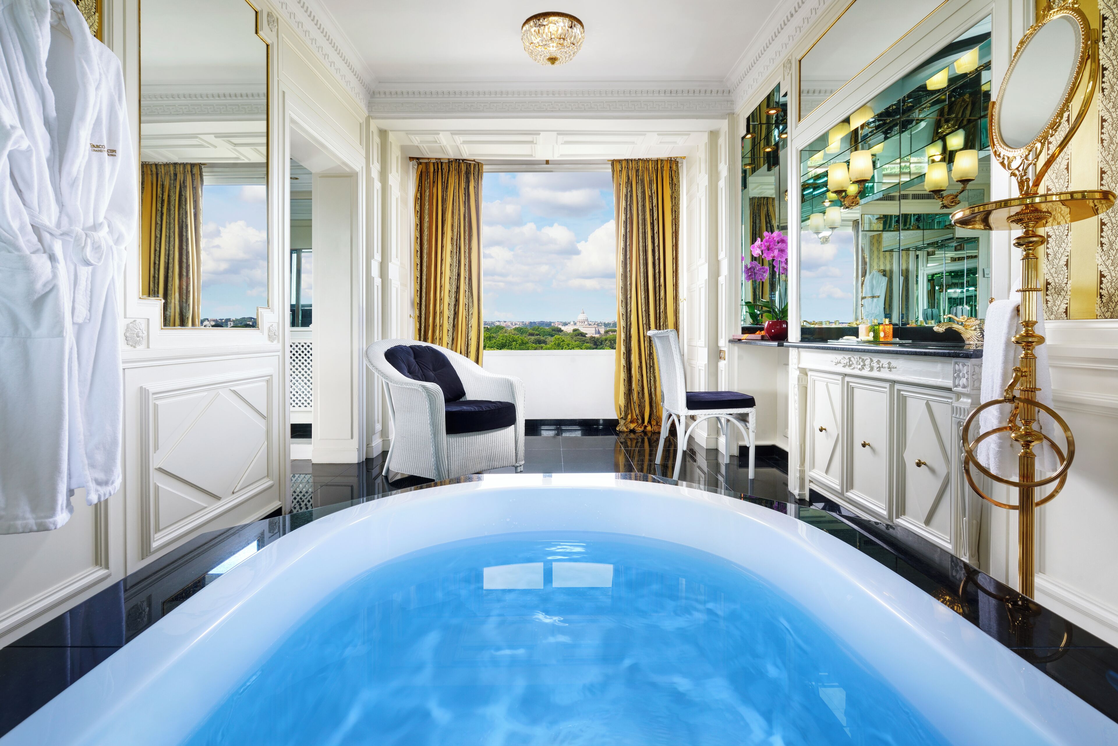 Ein luxuriöses Badezimmer mit einer großzügigen Badewanne, einem weißen Bademantel, einem Sessel und Blick auf die Stadt.