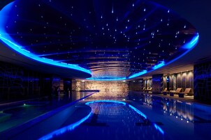 A modern indoor swimming pool with a curved ceiling and blue lighting.