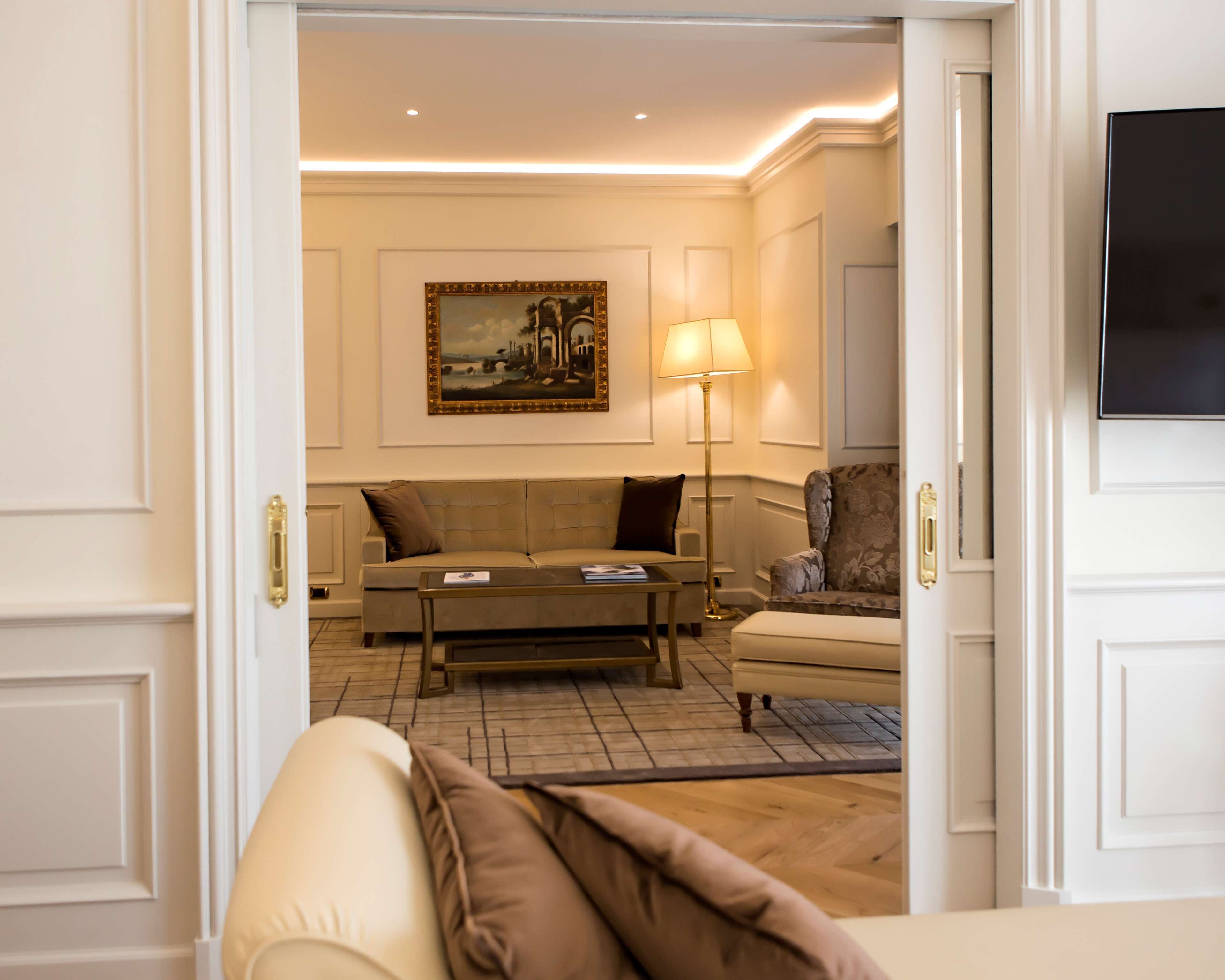 A well-lit living room with a sofa, armchair, and a coffee table. A painting is on the wall, and a lamp is on the floor.