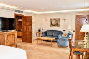 Ein geräumiges Wohnzimmer mit einem großen Flachbildfernseher, einem blauen Sofa, einem Holztisch und einem Essbereich mit einem Glastisch und Stühlen.