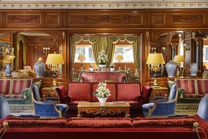 Un'elegante stanza con pannelli in legno decorati, un divano rosso, poltrone blu e un tavolino centrale con un vaso di fiori.