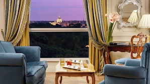 Habitación con vista a un paisaje urbano, que incluye una mesa con bebidas y aperitivos, dos sillones azules y un espejo en la pared.