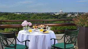 Una mesa dispuesta con alimentos para el desayuno, un jarrón con flores y una vista de un edificio con cúpula al fondo.