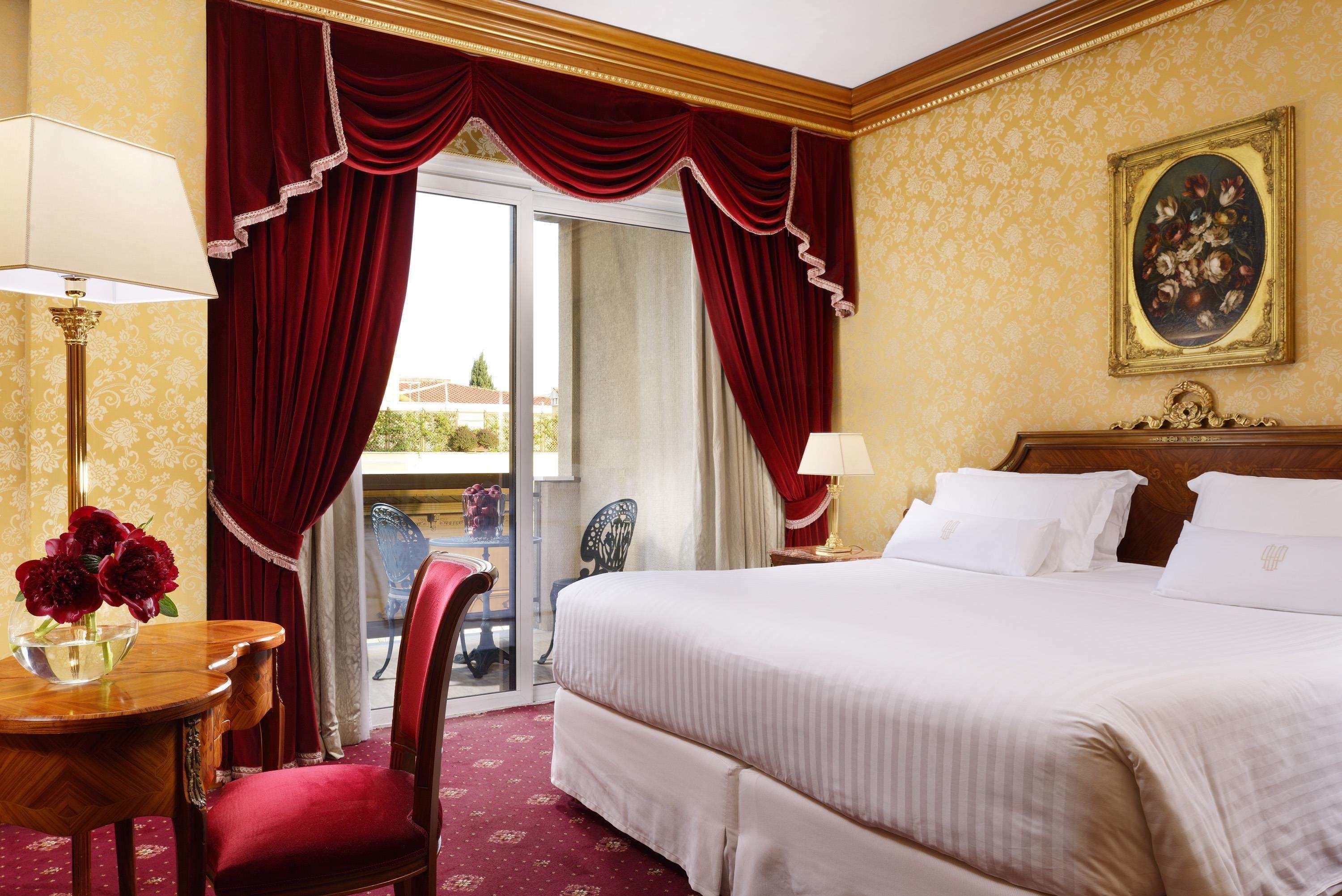 Een hotelkamer met een groot bed, een bureau met een lamp, een stoel en uitzicht door een glazen deur.