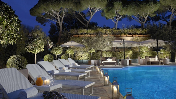 Zona de piscina con sillones de descanso, una mesa con una bebida y faroles.