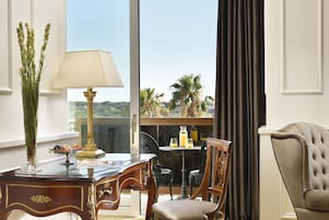 A room with a desk, a lamp, a chair, a table with drinks, and a view of palm trees.