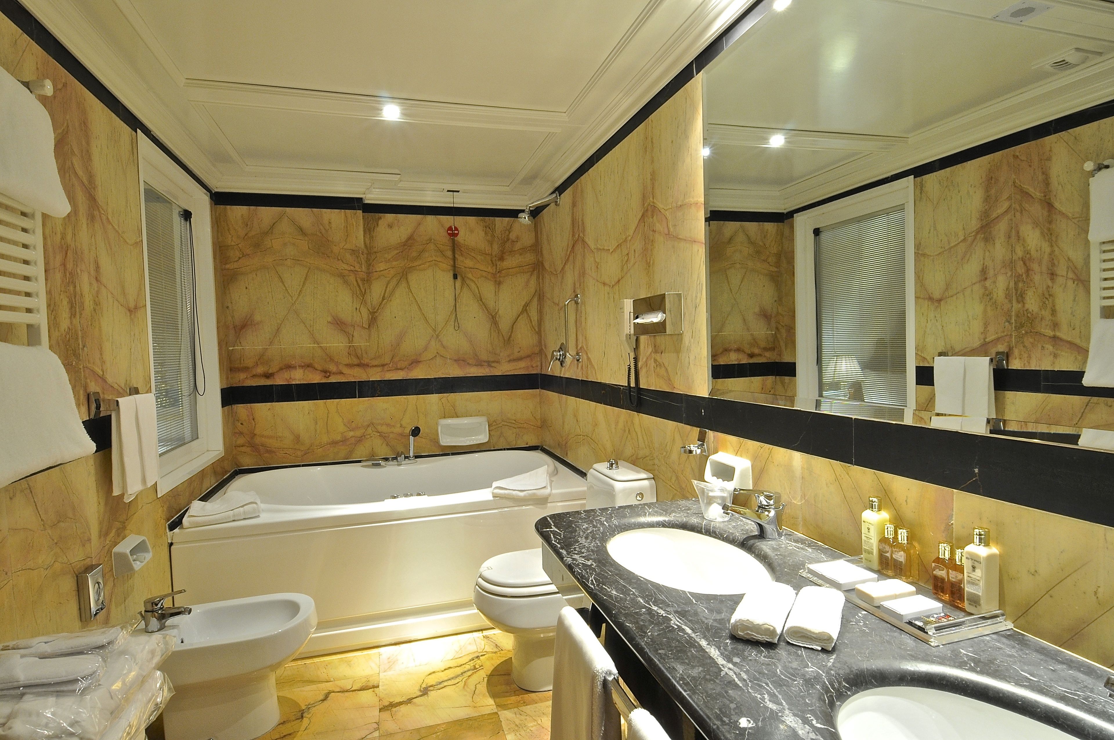 Un baño lujoso con pared de mármol, una bañera grande, lavamanos doble y un bidé.
