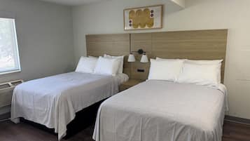 Habitación de hotel con dos camas, cabecera de madera, una obra de arte colgada en la pared y una ventana con persianas.