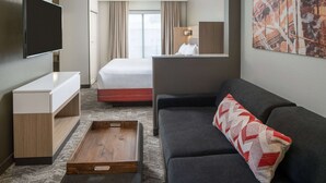 A hotel room with a flat-screen TV, a bed, a sofa, a wooden side table, and a large abstract painting on the wall. - Sonesta Select Nashville Airport Suites (Nashville)