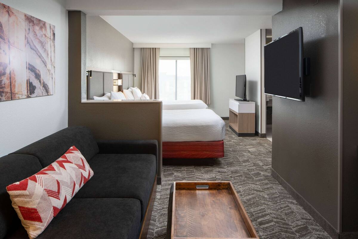 A hotel room with a sofa, a bed, a TV, and a wooden tray.