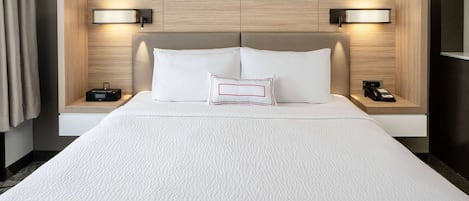 Quarto de hotel com uma cama grande, duas mesas de cabeceira com luminárias e cabeceira com iluminação embutida.