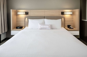 Quarto de hotel com uma cama grande, duas mesas de cabeceira com luminárias e cabeceira com iluminação embutida.