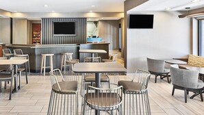 A modern restaurant with a bar area, multiple seating options including tables and chairs, and a flat-screen TV mounted on the wall.
