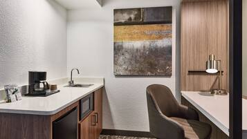 A compact kitchen with a coffee maker, sink, and a chair.