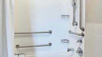 A modern bathroom with a bathtub, shower, and handrails.