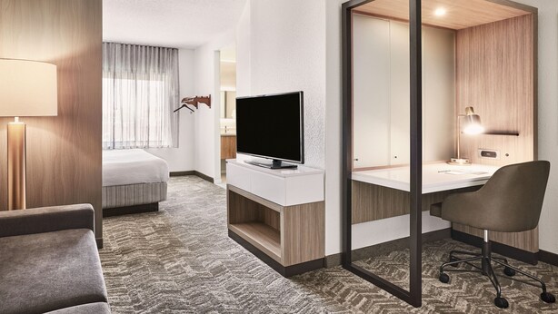 A hotel room with a bed, a TV, a desk, and a chair.