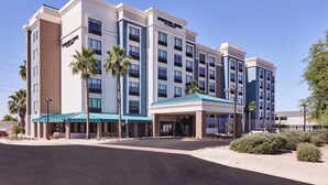 A multi-story hotel with a modern design, featuring a prominent entrance with a covered area and palm trees.