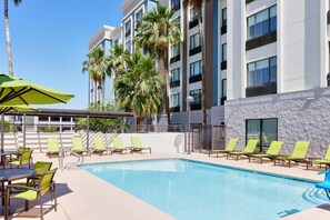 A hotel pool area with sun loungers, a table with chairs, and a covered seating area. - SpringHill Suites Phoenix Airport/Tempe (Tempe)