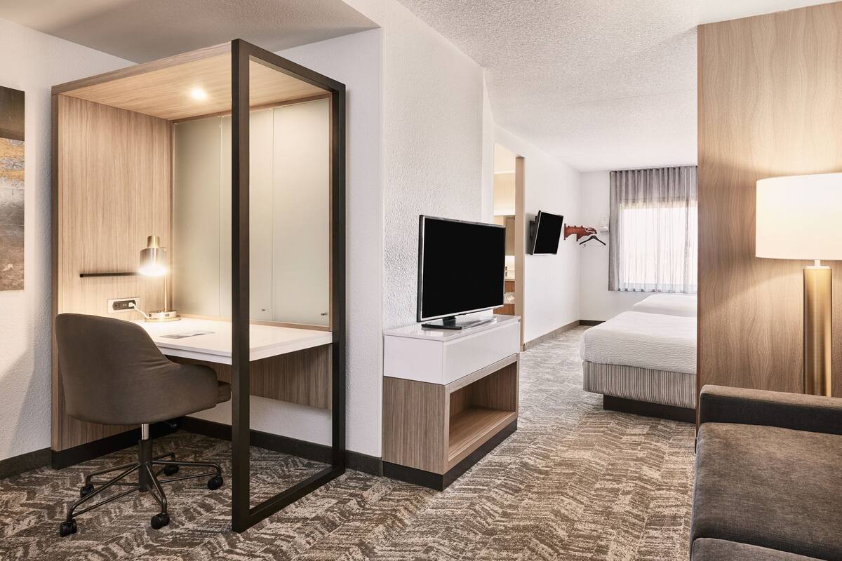 A hotel room with a desk, chair, TV, bed, and a mirror.