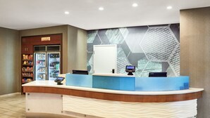 A reception desk with a digital kiosk, a refrigerator stocked with snacks, and a wall with geometric patterns.