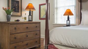 A bedroom with a wooden dresser, two lamps, a bed with white bedding, a window with blinds, and a framed map on the wall.