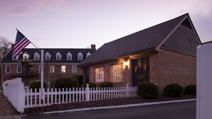 A brick house with a white picket fence, a flag, and a well-lit front door. - Fife And Drum Inn (Williamsburg)