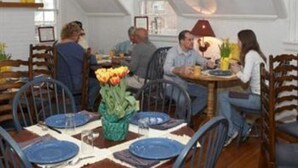 A dining area with round tables, chairs, and a central flower arrangement. - Fife And Drum Inn (Williamsburg)