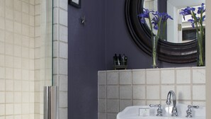 A bathroom with a glass shower enclosure, a pedestal sink, and a green stool with towels. - Fife And Drum Inn (Williamsburg)