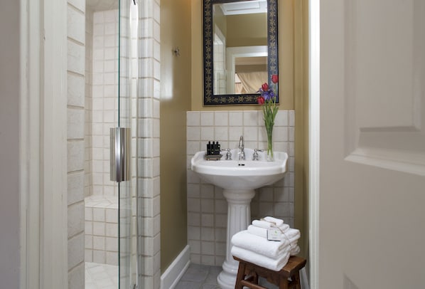 A bathroom with a glass shower enclosure, a pedestal sink, and a mirror above it. - Fife And Drum Inn (Williamsburg)