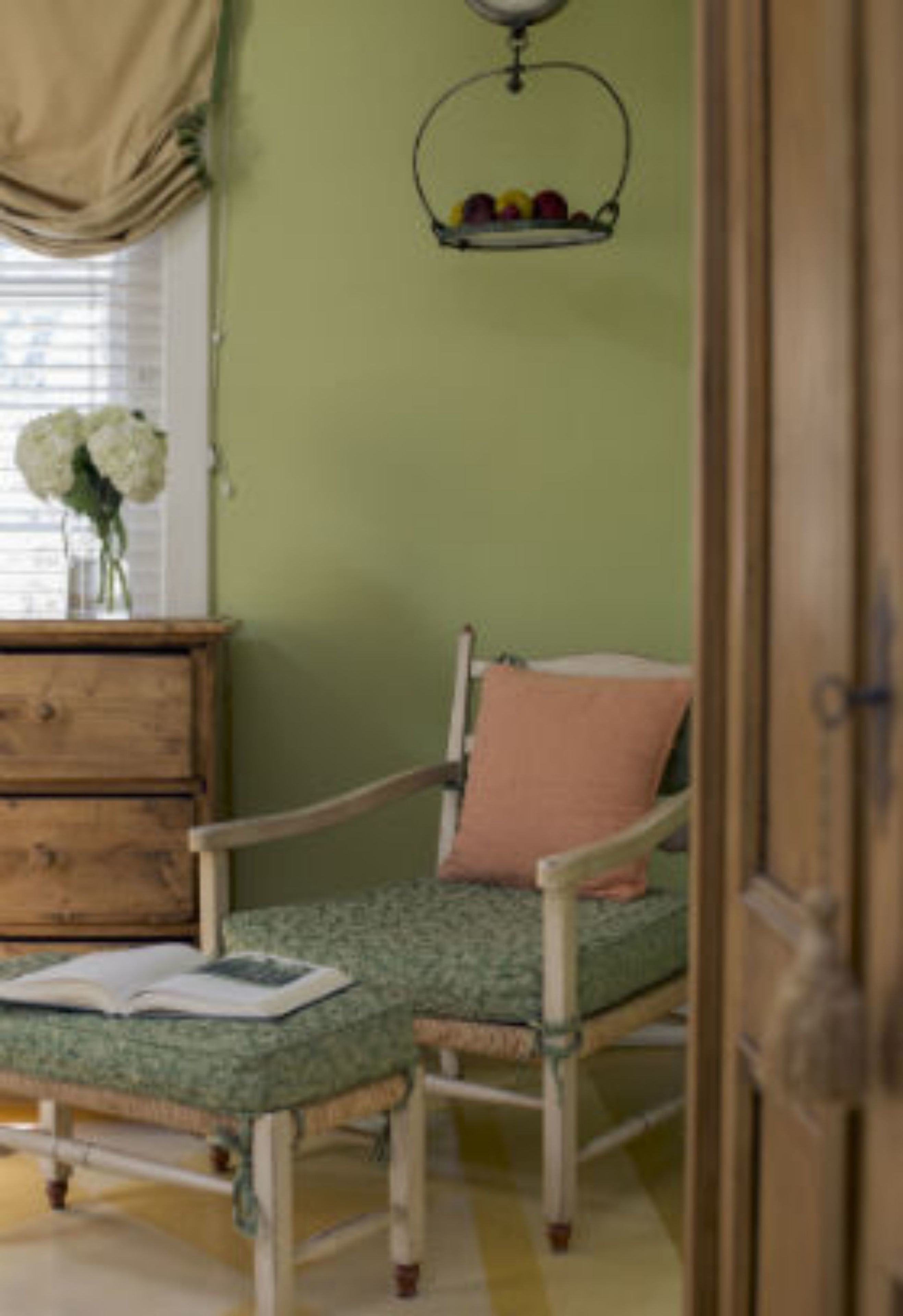 A room with a bed, a wooden dresser, a vase with flowers, and a wall-mounted fruit basket.
