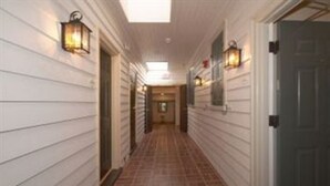 A hallway with white siding walls, a tiled floor, and wall-mounted lanterns. - Fife And Drum Inn (Williamsburg)