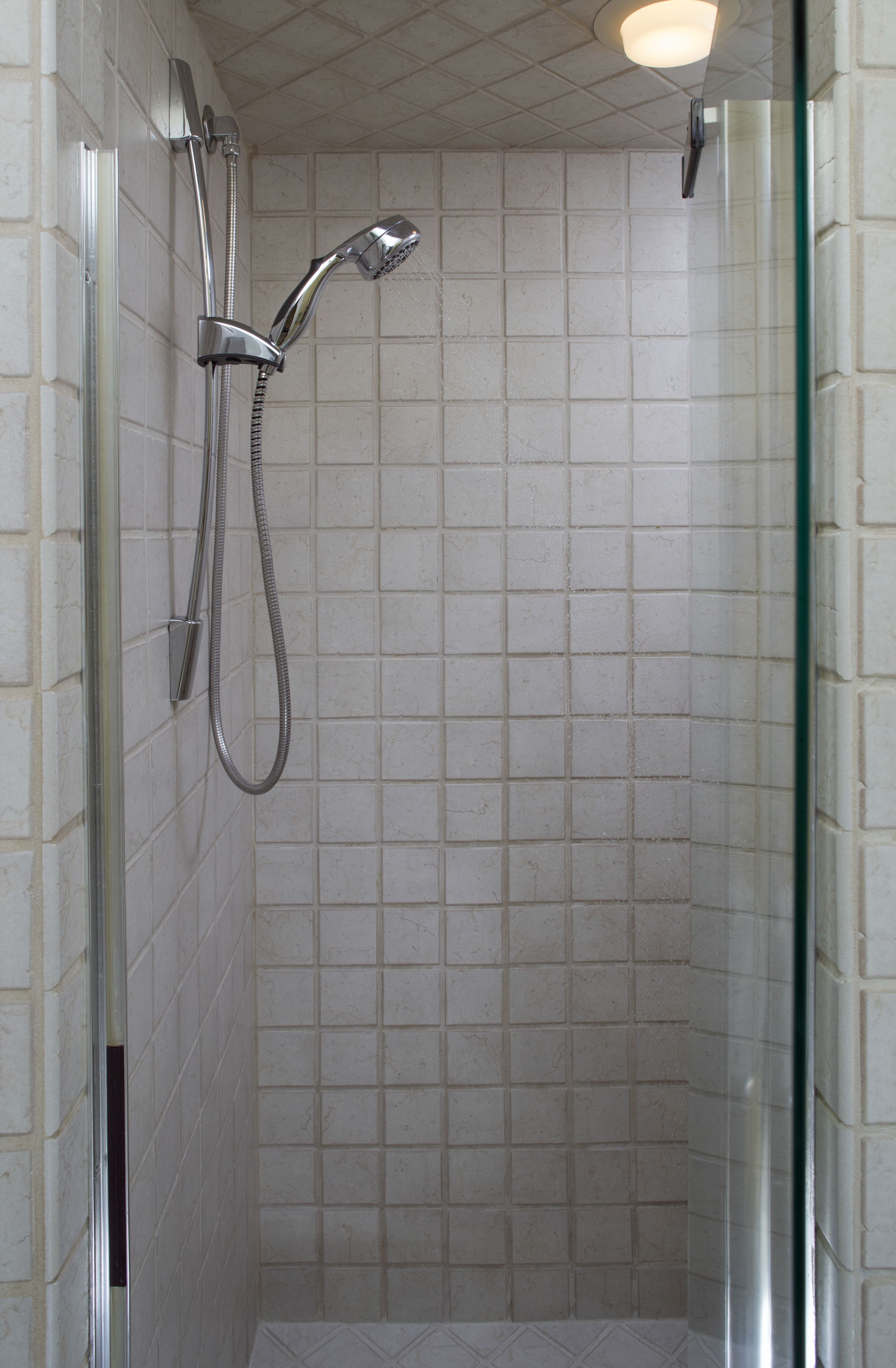 A glass-enclosed shower with a handheld showerhead and a fixed wall-mounted showerhead.