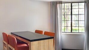 Una habitación con una mesa de madera y cuatro sillas naranjas, una ventana con cortinas y vistas al exterior.