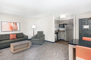 Un apartamento moderno con sala de estar, kitchenette y un sofá gris con un cojín rojo.
