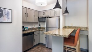 Una cocina moderna con electrodomésticos de acero inoxidable, encimera de granito y una silla de madera.