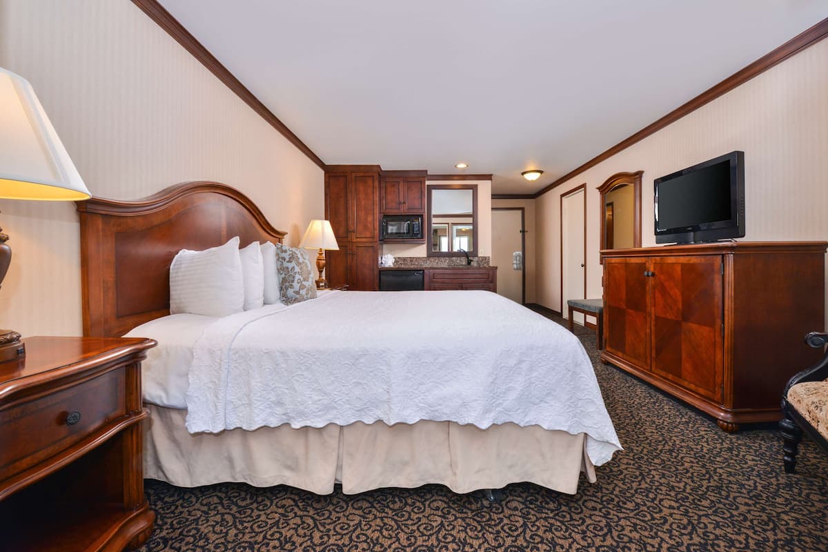 Habitación de hotel con una cama grande, cabecera de madera, un escritorio con lámpara, televisión y armario.