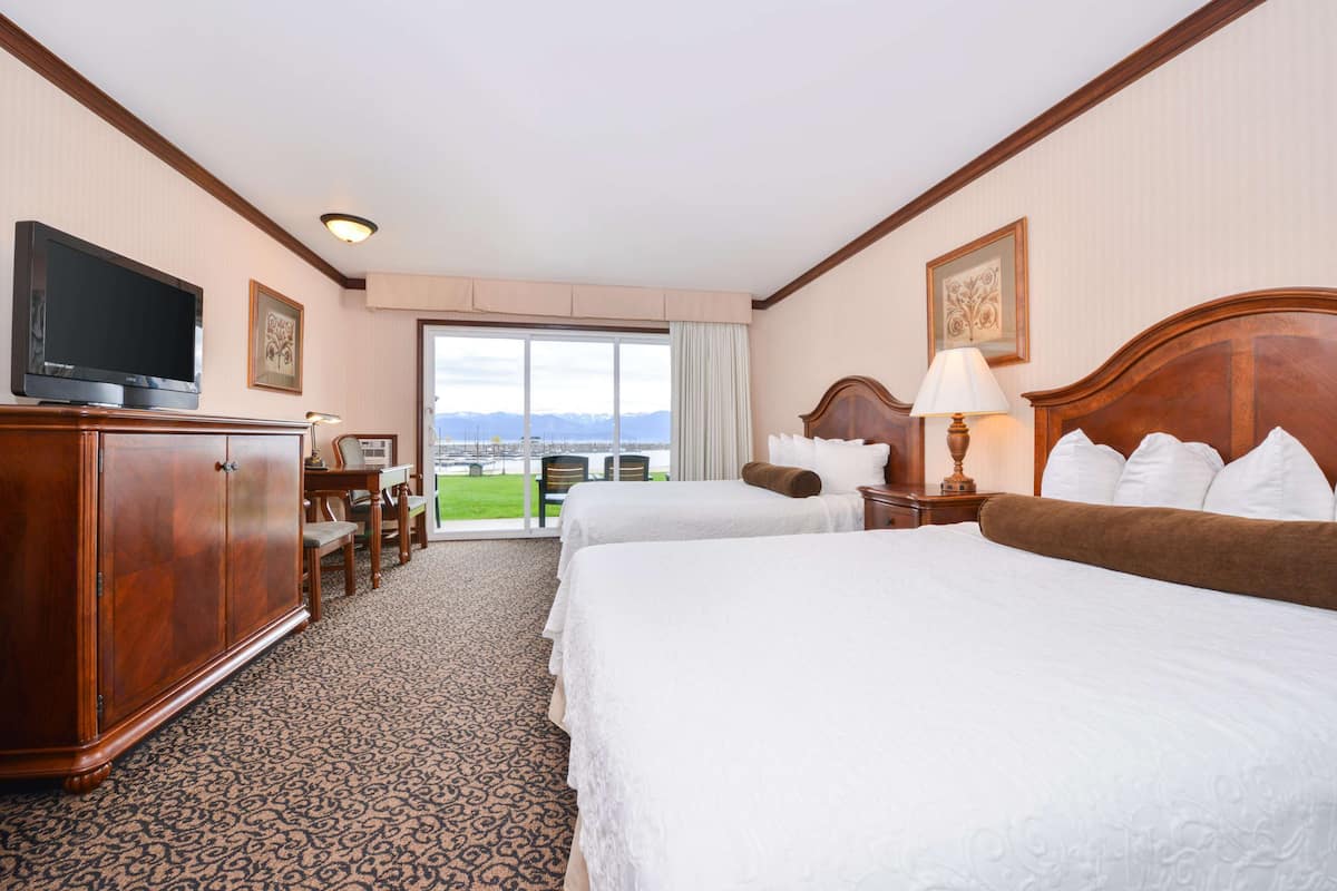 Habitación de hotel con dos camas, televisión, escritorio y vistas a montañas.