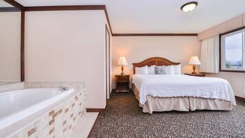 A hotel room with a large bathtub, a double bed with white linens, two bedside lamps, and a patterned carpet.