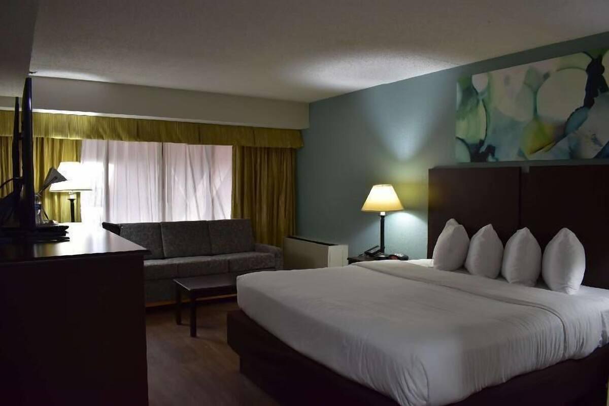 Ein Hotelzimmer mit Bett, Sofa, Schreibtisch, Lampe und einem Bild an der Wand.